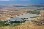 Bird's eye view over a largely unvegetated plain with a lake. In the distance a mountain range is visible.